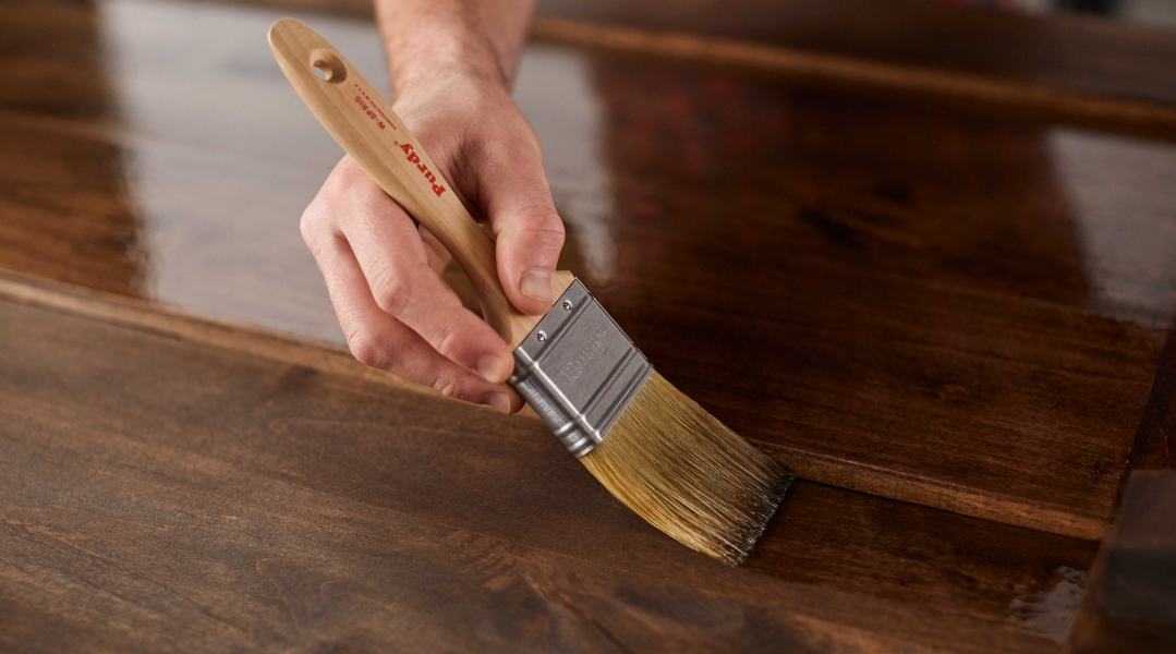 A pro painter applies stain to the surface of a wooden table